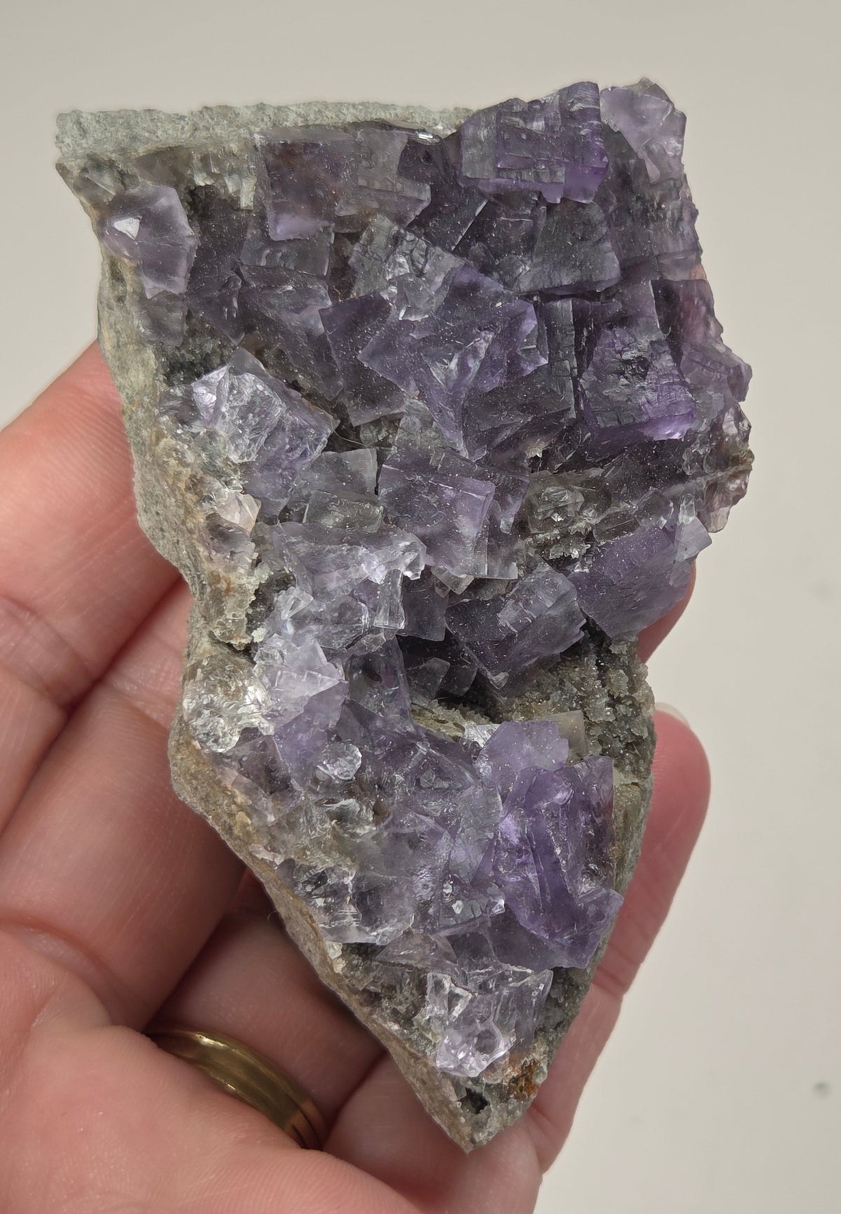 A raw fluorite crystal cluster with purple crystalline formations attached to a gray matrix, photographed on a plain white background.