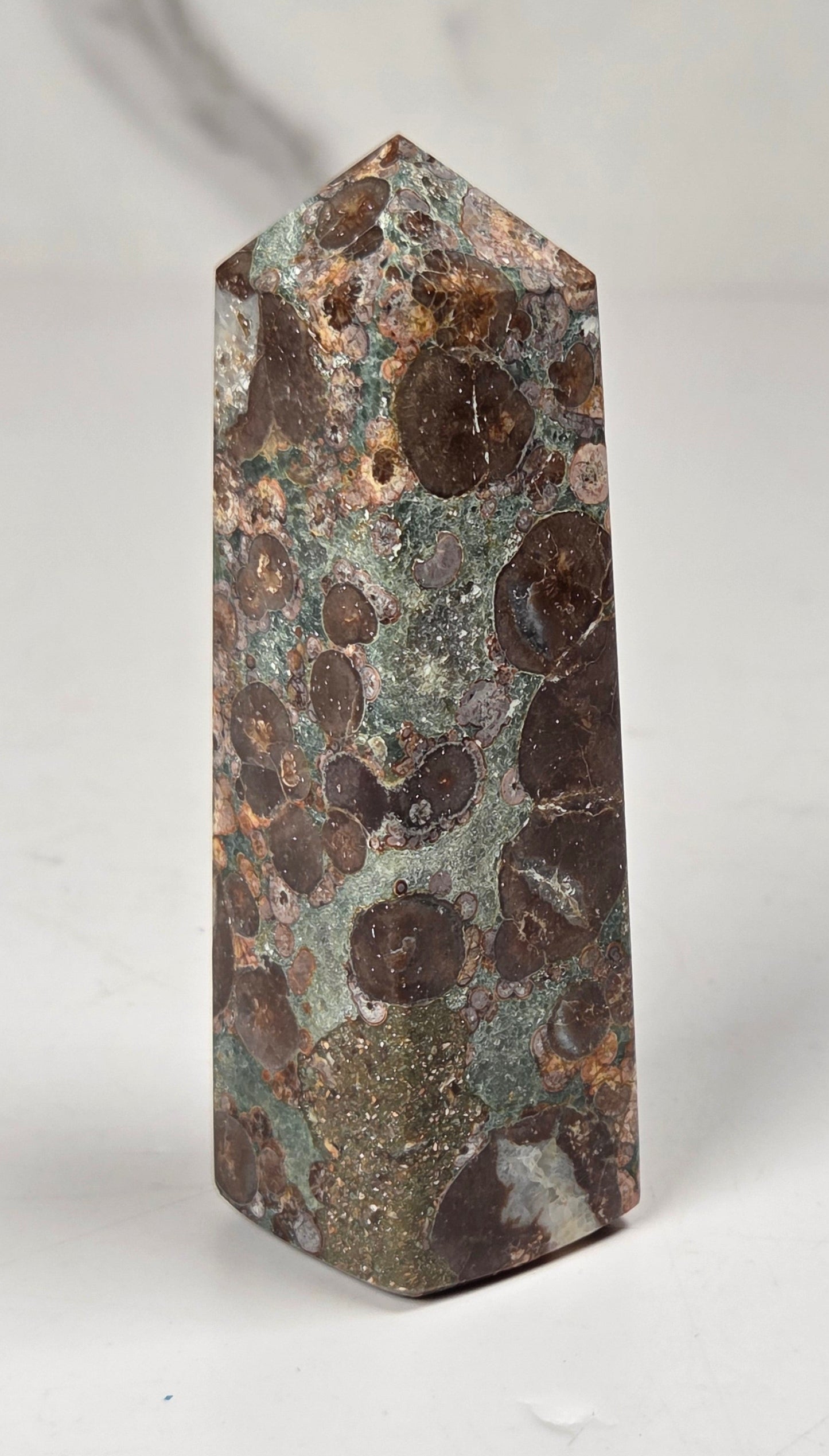 A natural jasper stone crystal tower with a pointed top, featuring a mottled pattern of brown, copper, and greenish-gray mineral deposits on a white background.