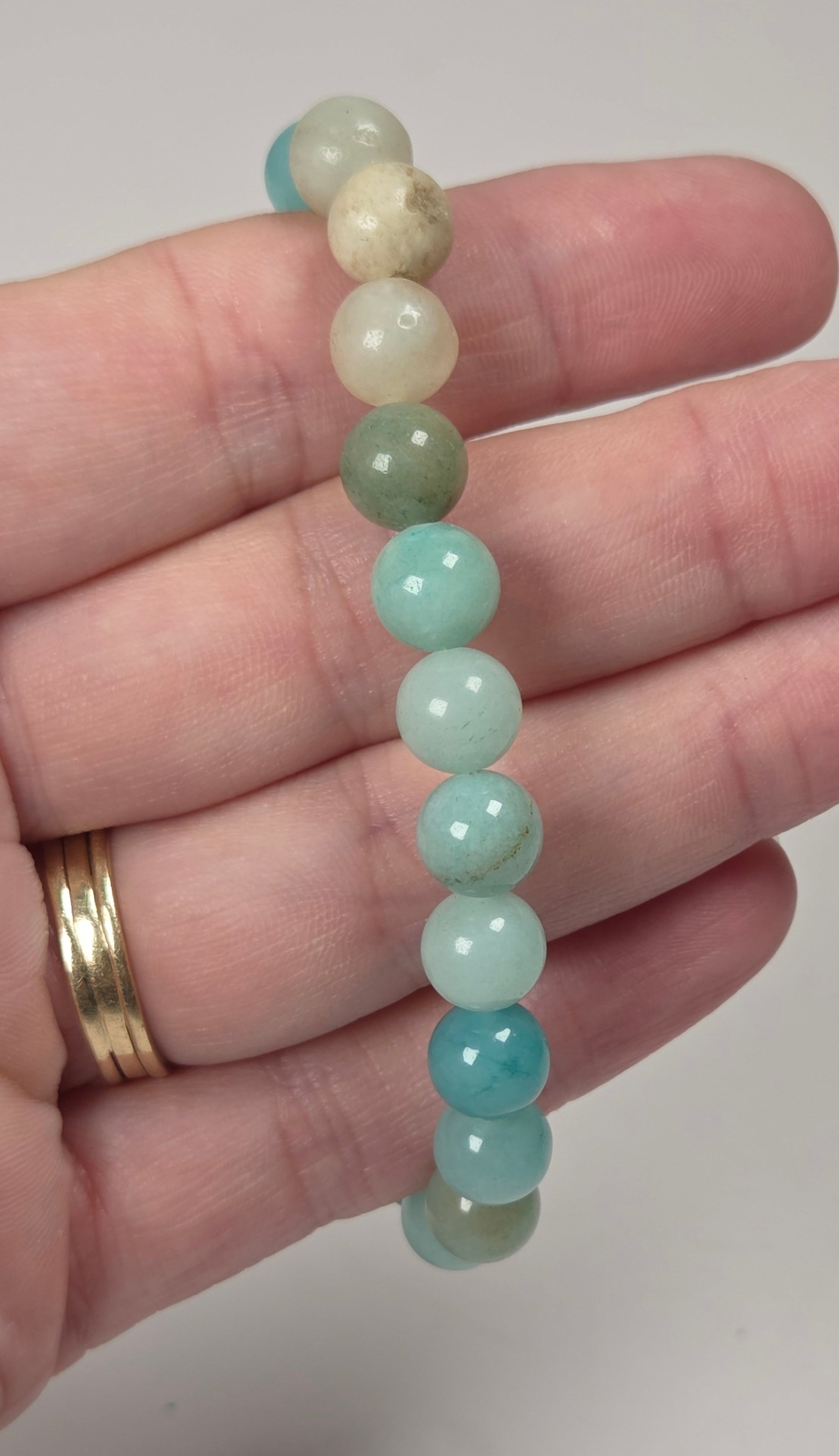 A beaded stretch bracelet made of smooth, polished round beads in shades of light blue, mint green, and cream, held in a person's hand.