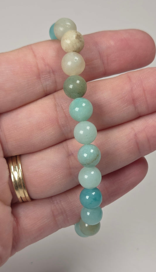 A beaded stretch bracelet made of smooth, polished round beads in shades of light blue, mint green, and cream, held in a person's hand.