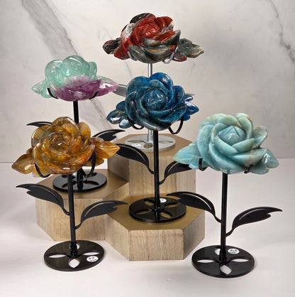 Set of 5 crystal rose carvings in a variety  of materials and colors, set on black metal stands with leaves on a wooden stand against a white background