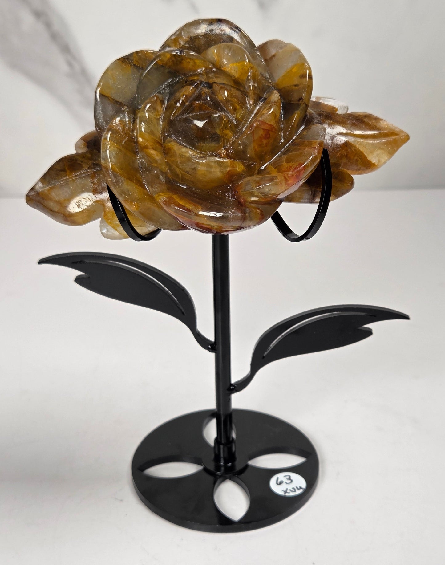 Golden Healer Crystal rose carving set on a black metal stand with leaves against a white background