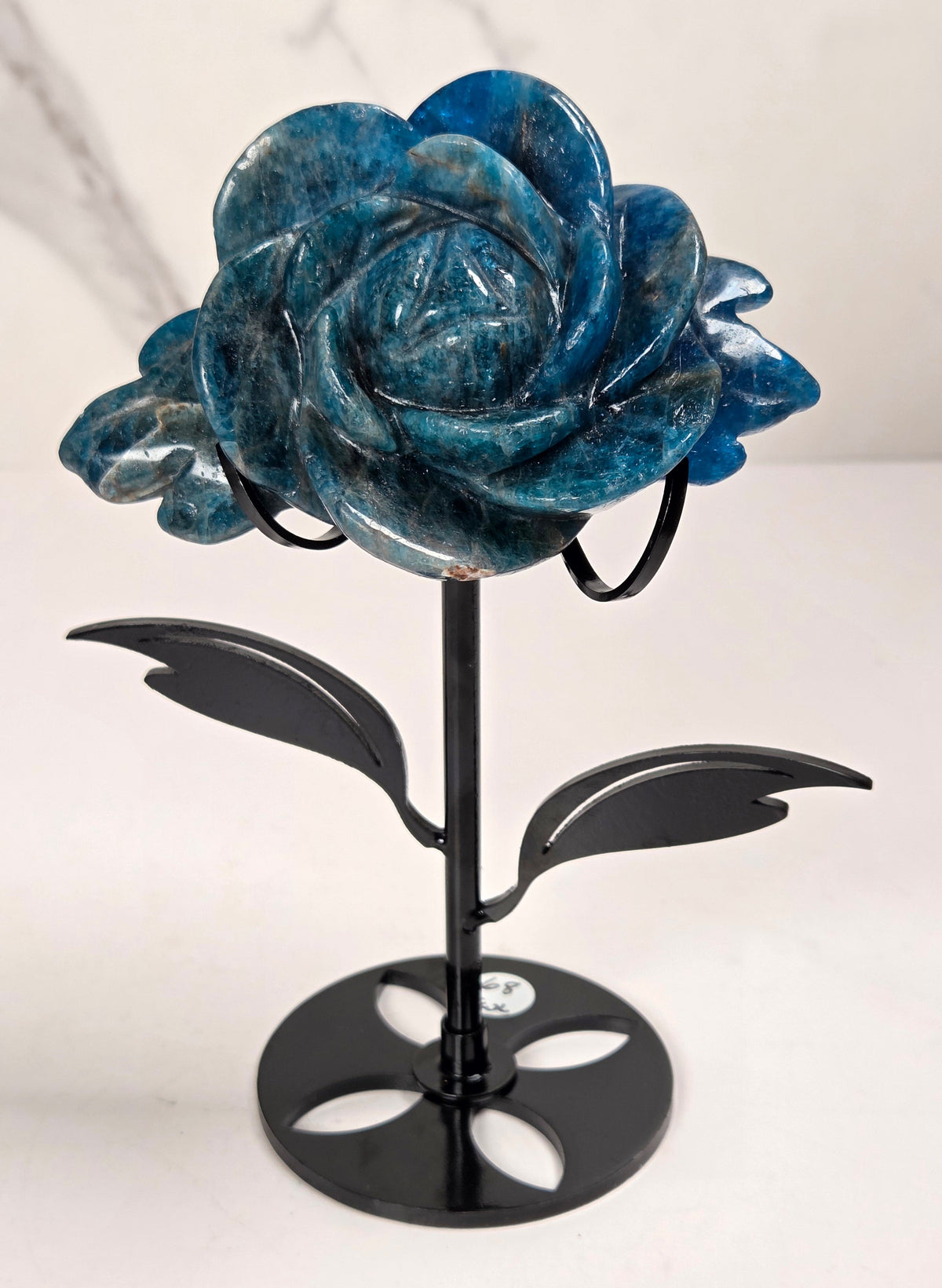 Blue Apatite Crystal rose carving set on a black metal stand with leaves against a white background