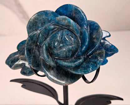 Blue Apatite Crystal rose carving set on a black metal stand with leaves against a white background