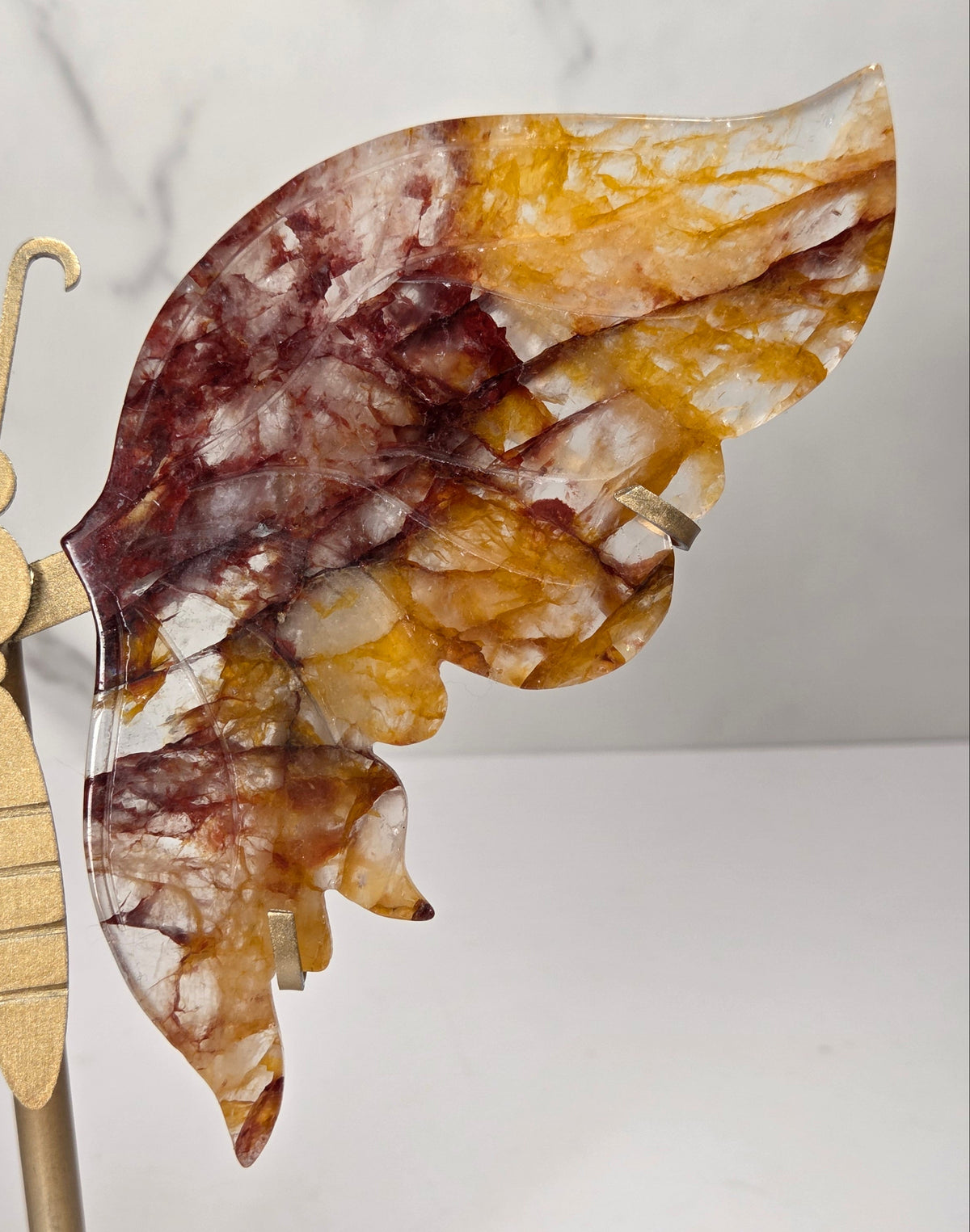 A decorative butterfly wall sculpture with marbled amber, brown, and cream wings mounted on a gold-toned metal stand against a white marble-patterned background.