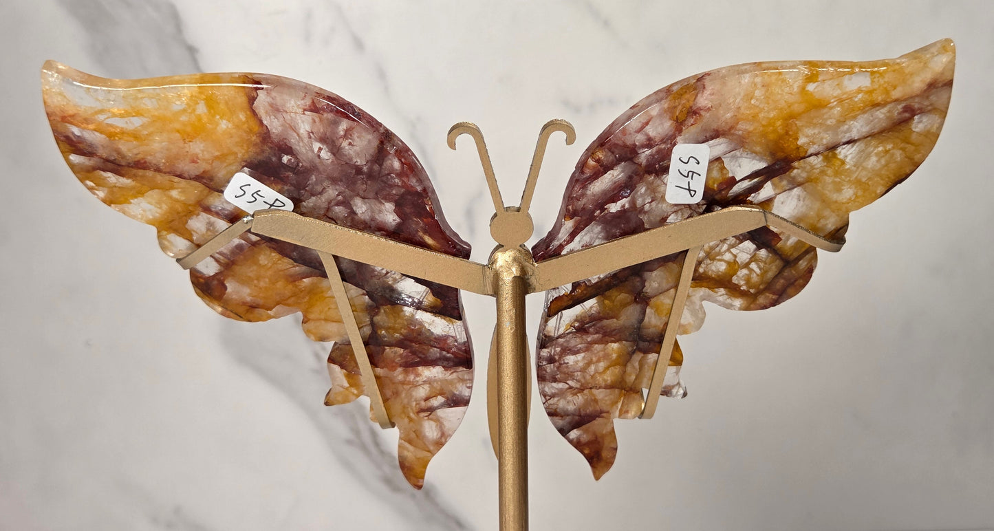 A butterfly-shaped wall art piece with marbled amber, brown, and cream wings mounted on a gold-toned metal stand, photographed against a light marble-patterned background.