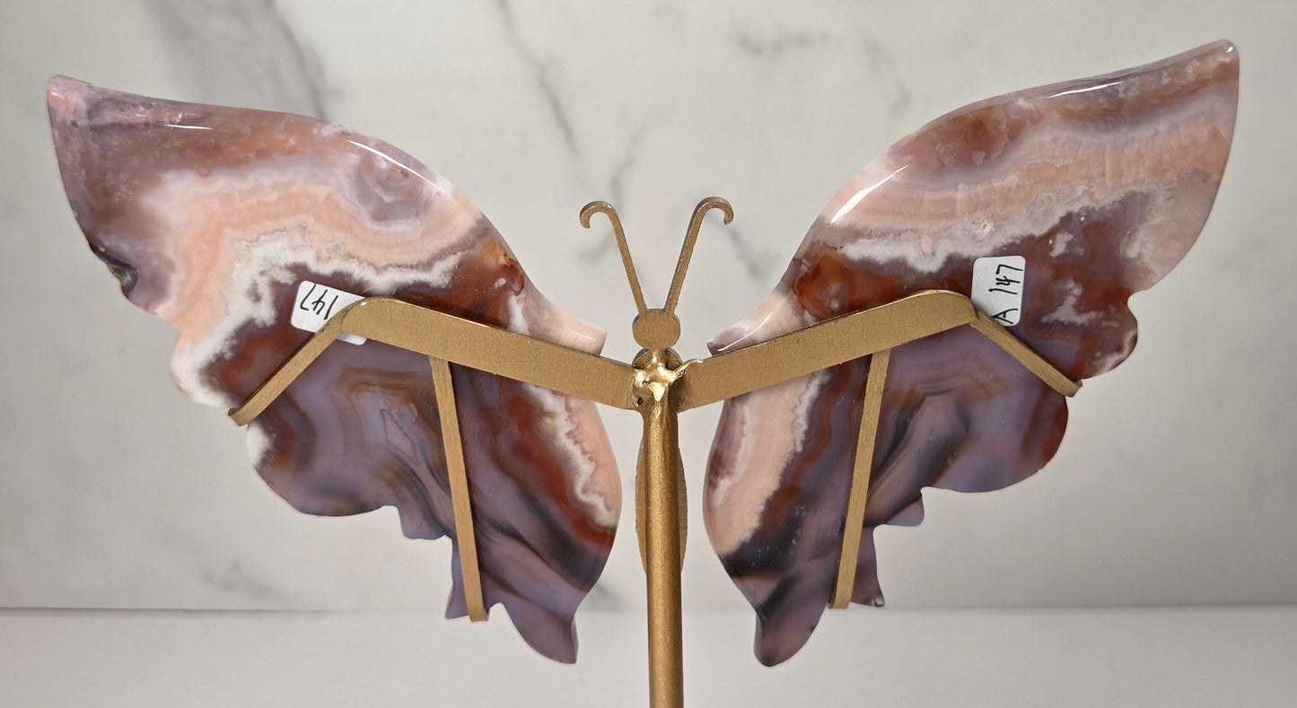 A butterfly-shaped jewelry display stand made from agate-patterned wings in shades of purple, brown, and peach, mounted on a gold-tone metal stand with a round base.