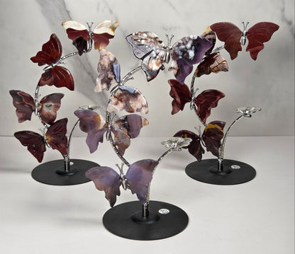 Set of 3 decorative metal sculpture of four butterfly-like figures arranged along a flowering stem on a round black base, photographed against a light marble-pattern backdrop.