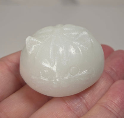 A small carved white stone cat figurine resting on a person's hand, with a gold ring visible on the ring finger.