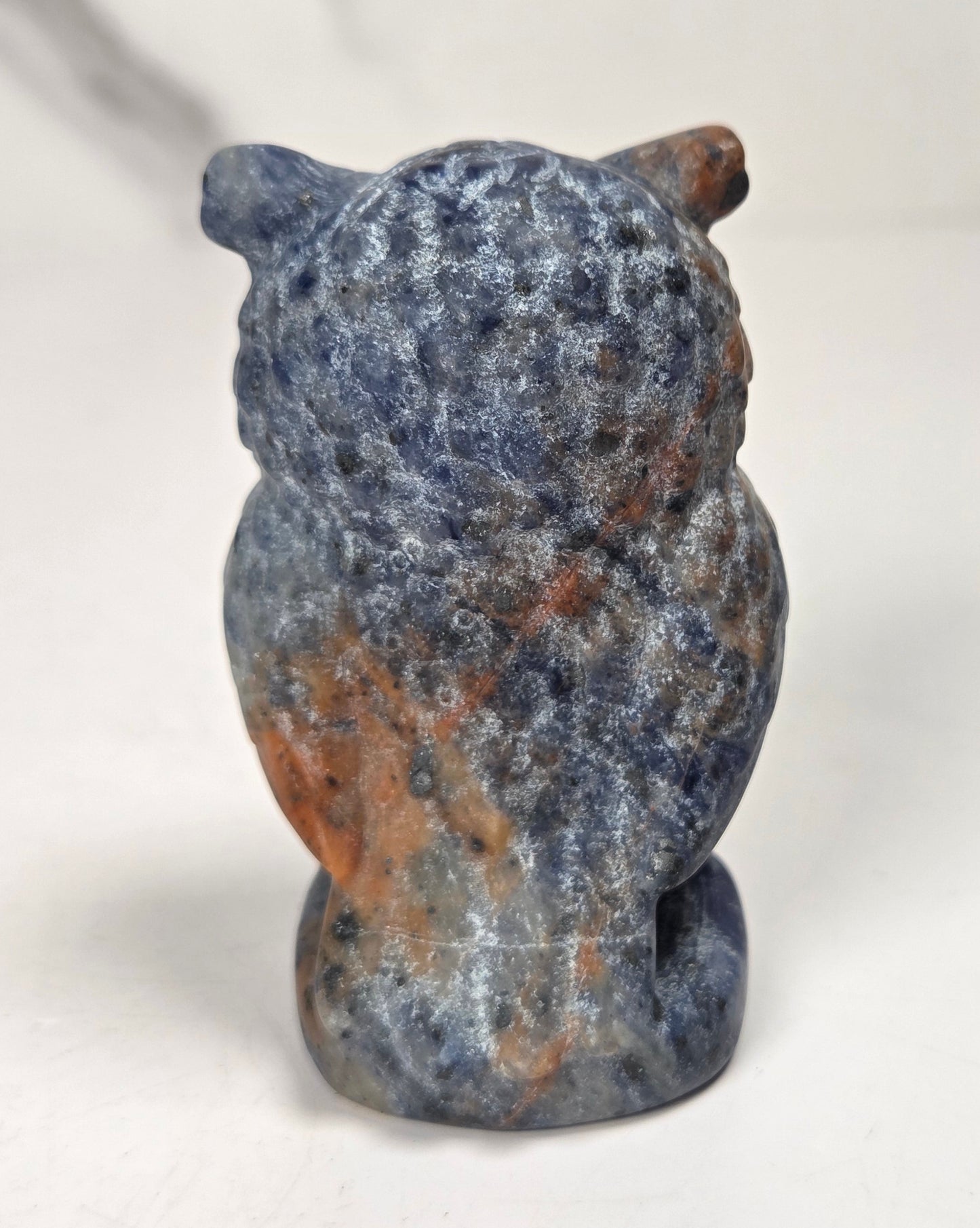 A small carved stone owl figurine shown from the back, made of mottled blue and orange stone, photographed on a plain light background.