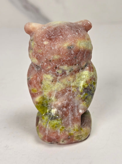 A small carved stone owl figurine with a mottled pinkish-red, green, and cream marbled pattern, standing on a light gray surface.