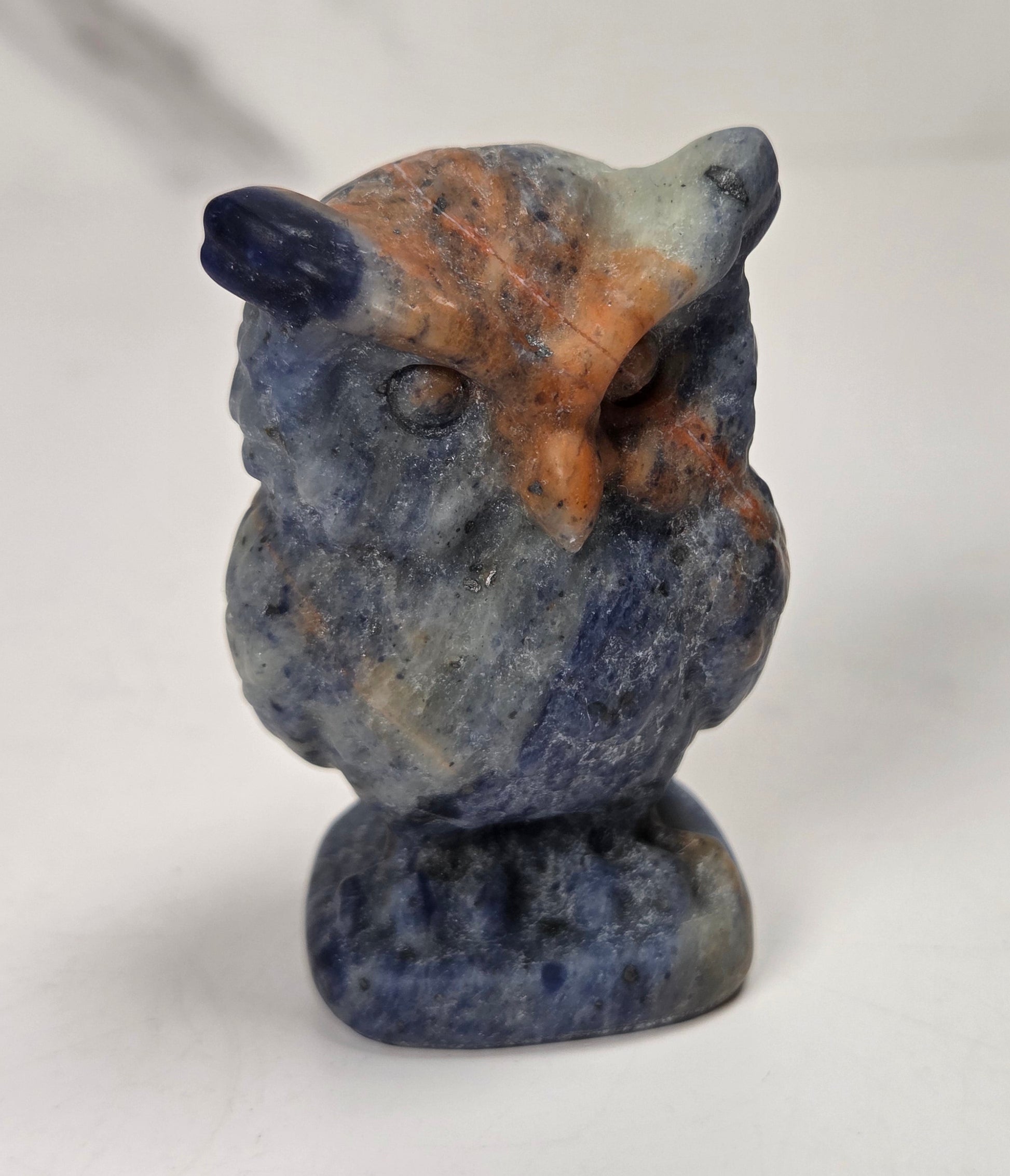 A small carved owl figurine made of blue and orange stone, standing on a matching stone base against a plain light background.