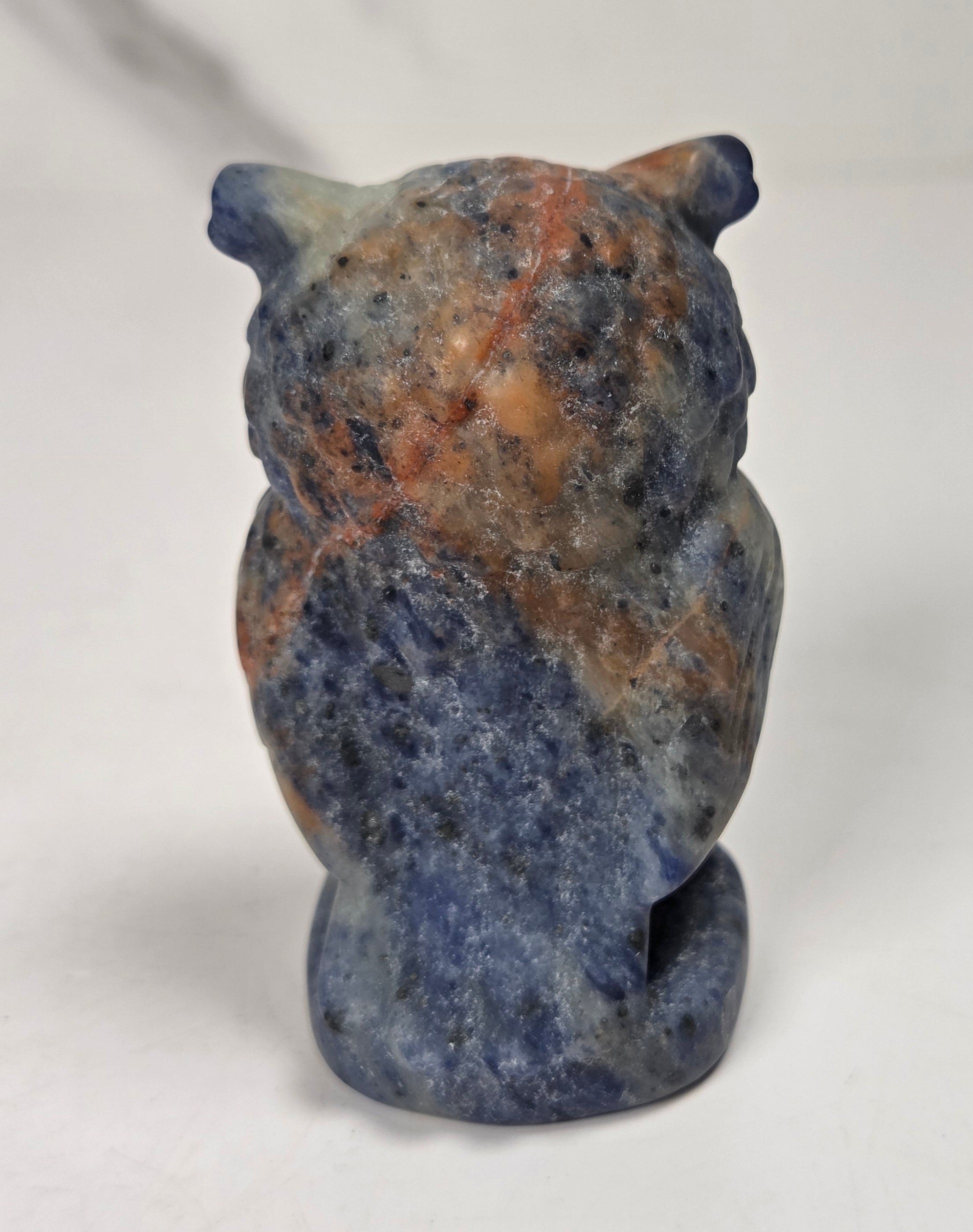 A small carved owl figurine made from blue and orange marbled stone, standing upright against a plain light gray background.