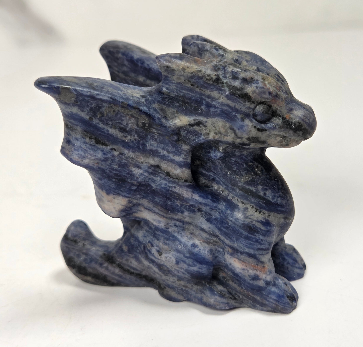 A small dragon figurine carved from blue lapis lazuli stone, standing on a plain white surface.