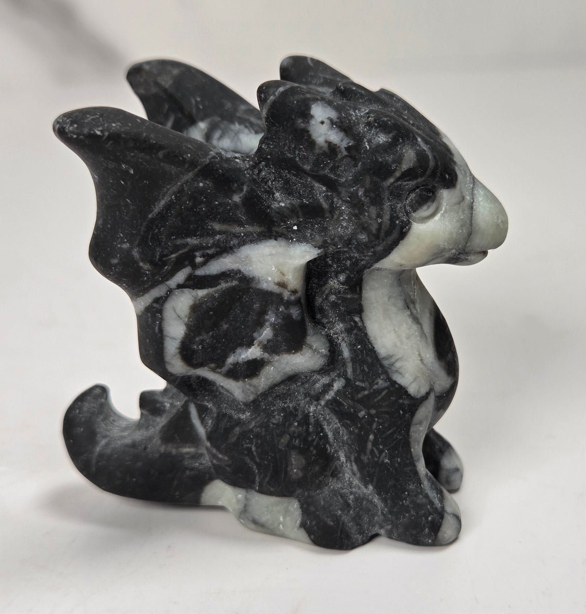 A small carved dragon figurine made from black and white marbled stone, shown from the side on a plain light background.