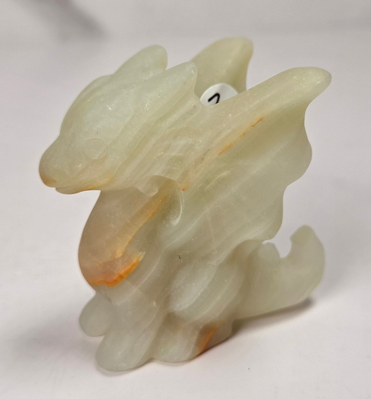 A small carved dragon figurine made of pale translucent stone with warm orange-brown inclusions, photographed on a plain light background.