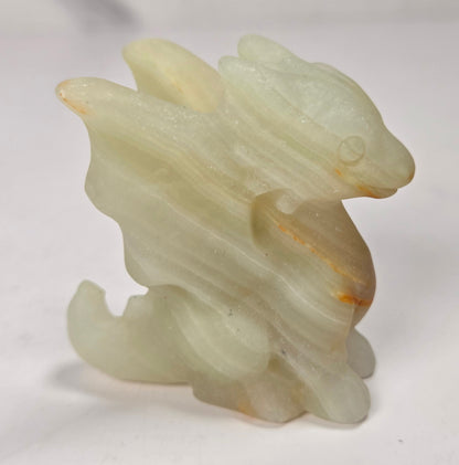 A small carved figurine of a stylized animal, likely a rabbit or dragon, made from pale translucent stone with subtle orange-brown inclusions, photographed on a plain light background.