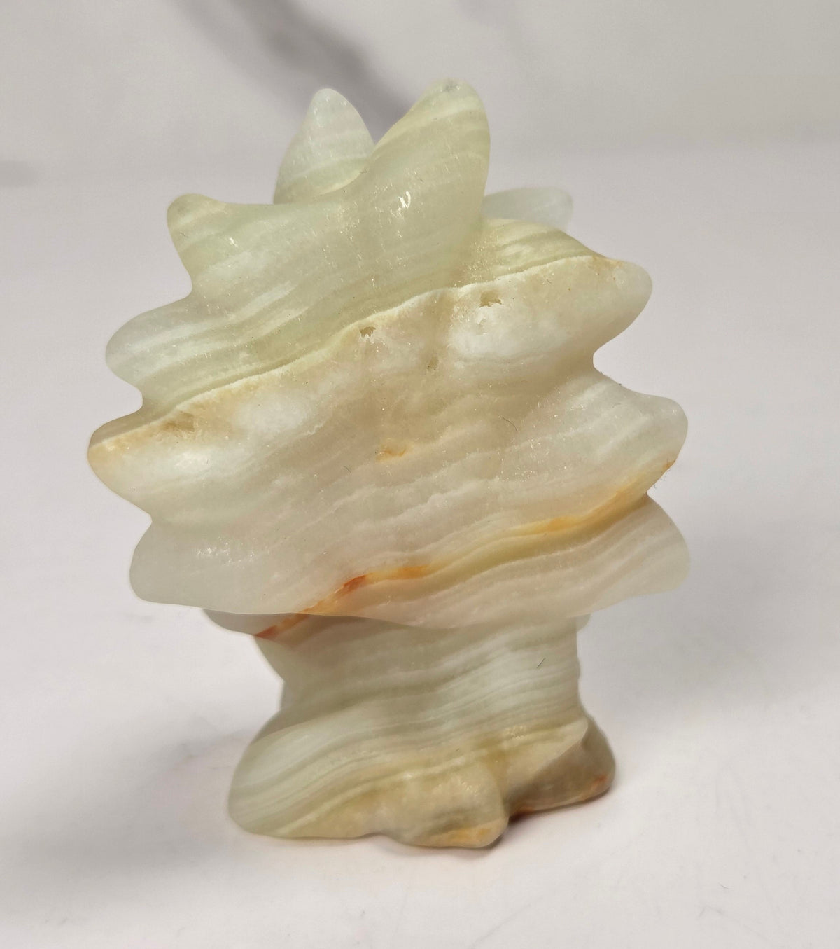 A small carved stone sculpture shaped like a spiral shell, made from pale cream and beige stone with subtle warm brown highlights, set against a light gray and white marble-patterned background.