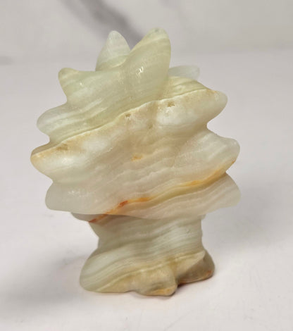 A small carved stone sculpture shaped like a spiral shell, made from pale cream and beige stone with subtle warm brown highlights, set against a light gray and white marble-patterned background.