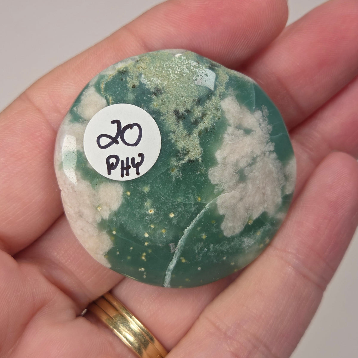A hand holding a polished green and white marbled stone with a small white sticker that reads '20 PHY'.