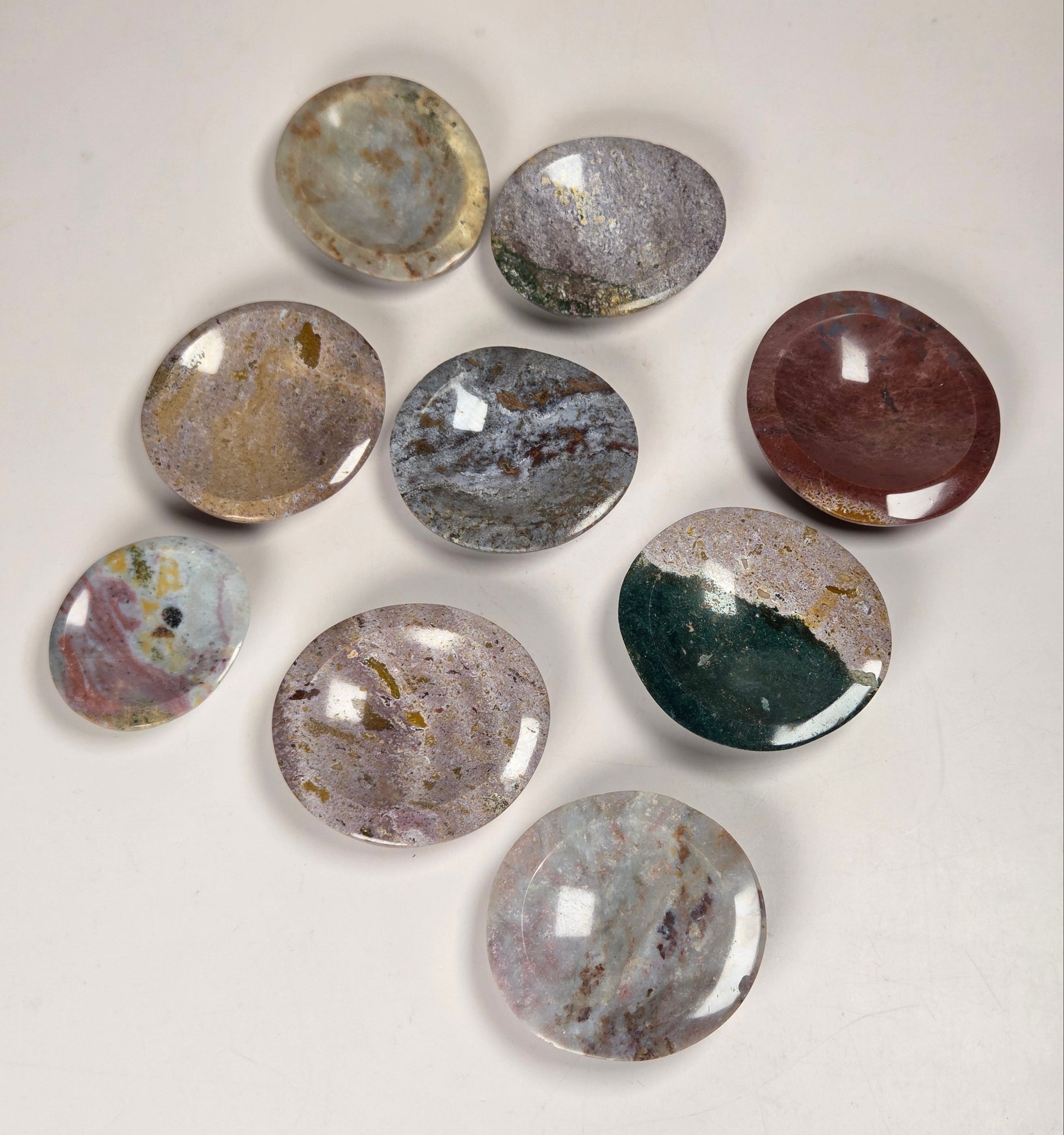Nine polished oval gemstone cabochons in various colors and patterns, arranged on a plain off-white background.