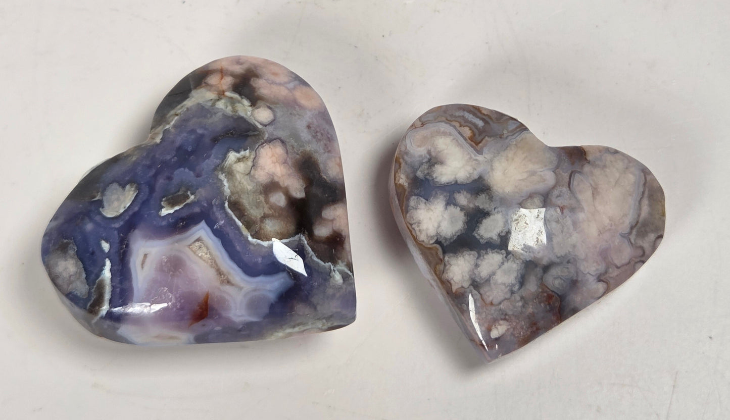 Two polished heart-shaped agate stones with marbled purple, blue, white, and gray patterns, displayed on a light gray surface.