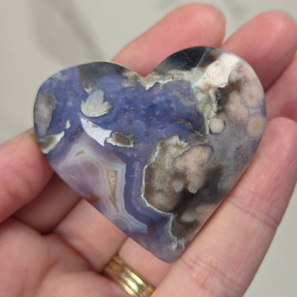 A heart-shaped polished stone with marbled blue, purple, gray, white, and brown patterns, held in a person's hand.