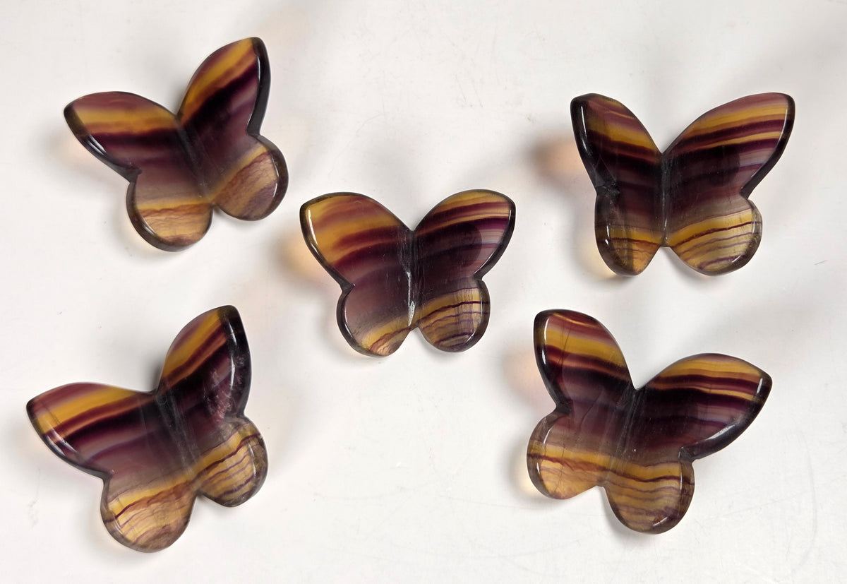 Five butterfly-shaped wall hooks made of striped amber, brown, and purple wood, arranged on a plain off-white background.