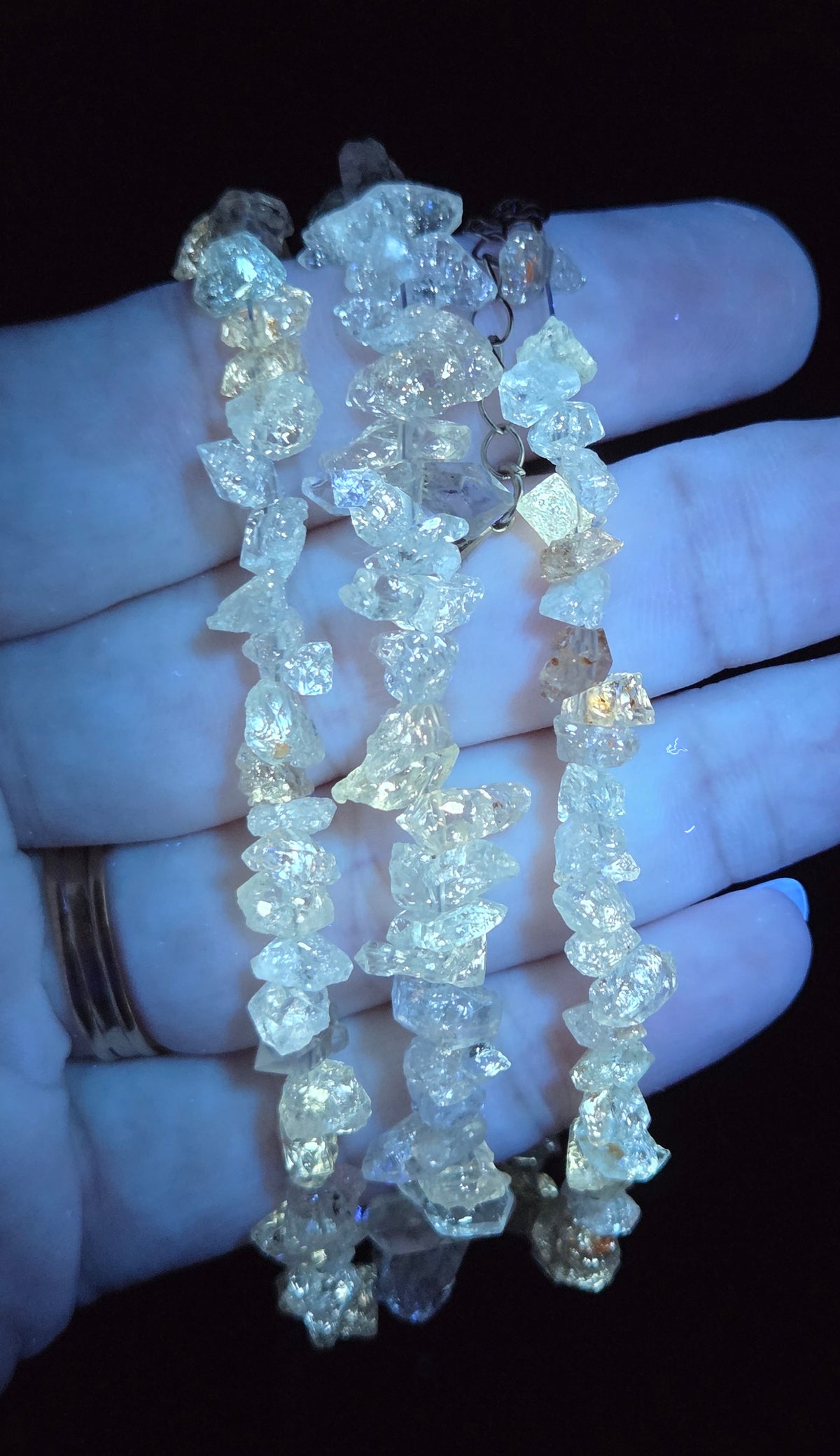 Three strands of raw, irregular clear quartz crystal beads held in a person's hand against a black background.