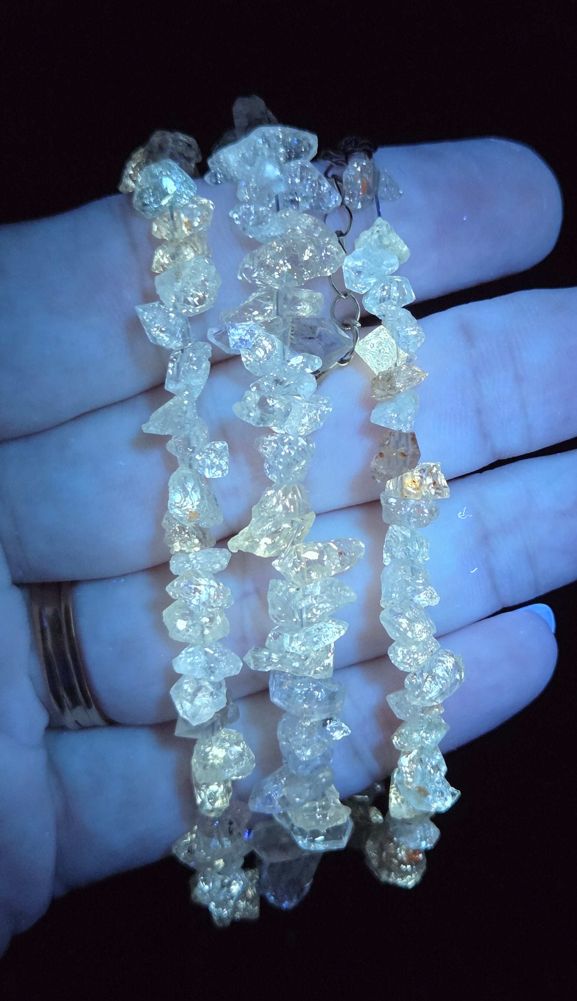 Three strands of raw, irregular clear quartz crystal beads held in a person's hand against a black background.