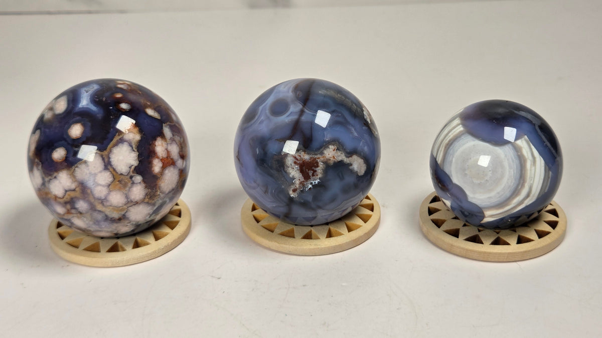 Three polished agate crystal spheres in various natural patterns, each resting on a small triangular wooden stand, displayed on a light surface.