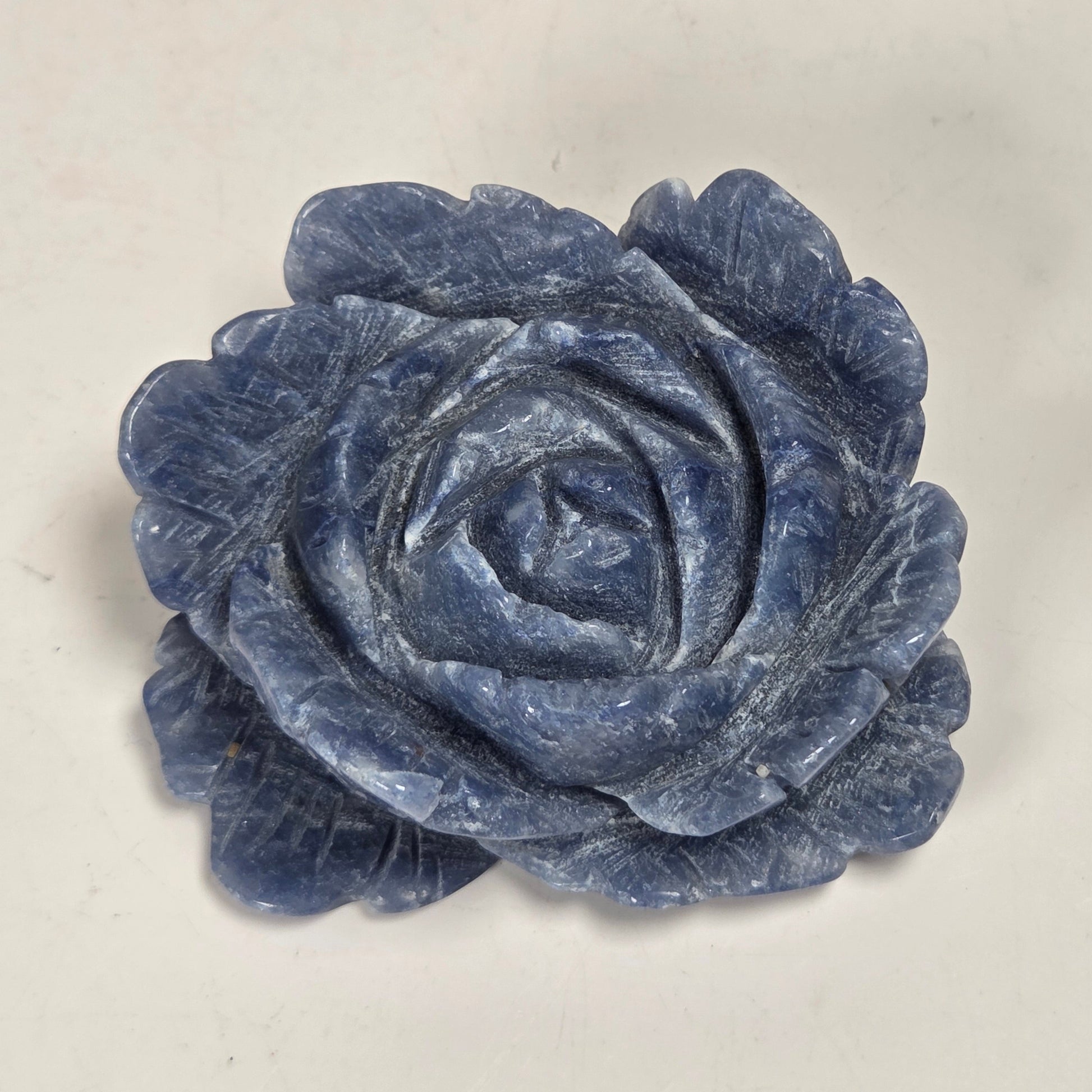 A carved blue rose-shaped object, likely a decorative sculpture or jewelry piece, shown on a plain off-white background.