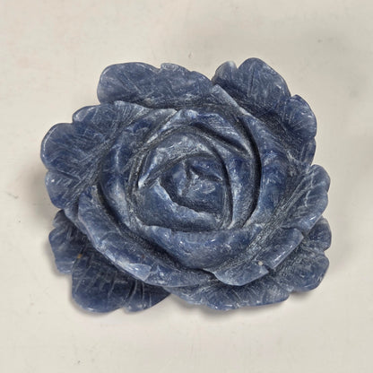 A carved blue rose-shaped object, likely a decorative sculpture or jewelry piece, shown on a plain off-white background.