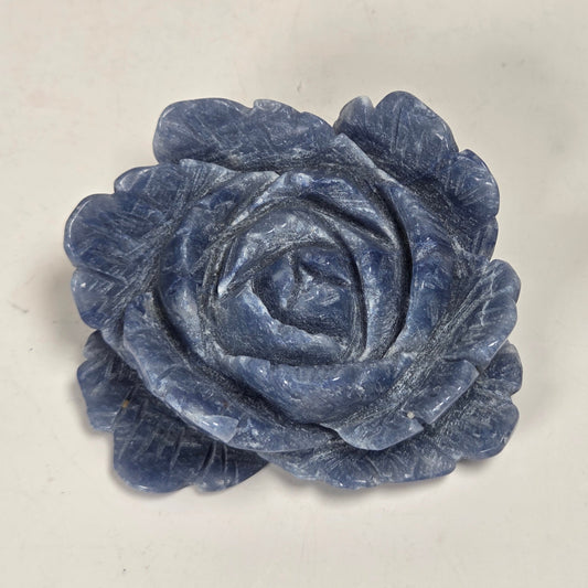 A carved blue rose-shaped object, likely a decorative sculpture or jewelry piece, shown on a plain off-white background.