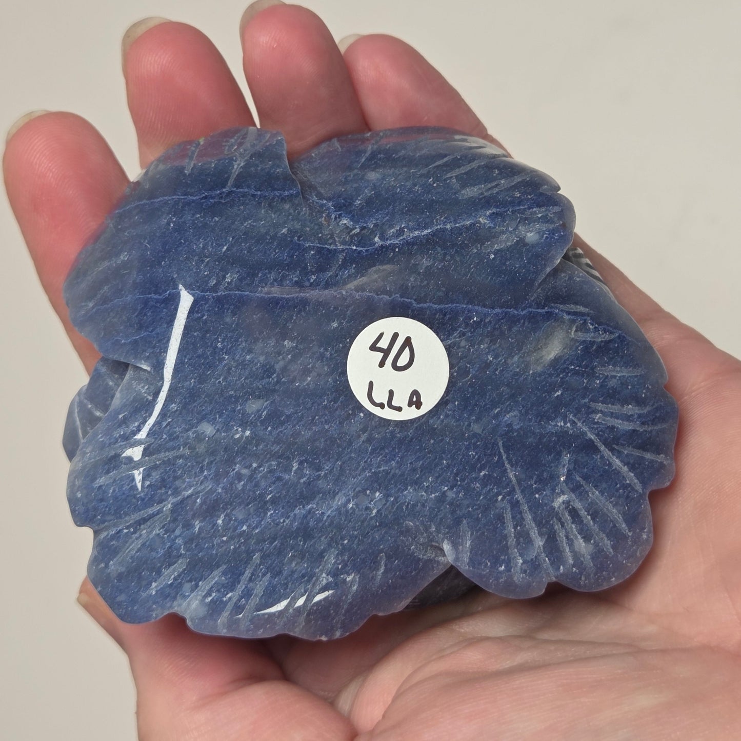A hand holding a carved blue stone object with a small white sticker that reads '4D'.