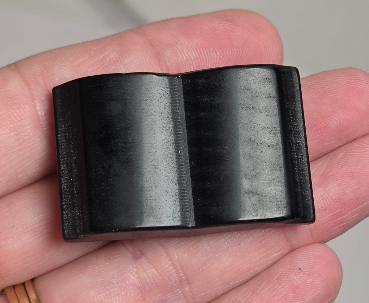 A black rectangular plastic component with a molded center ridge, held in a person's hand.