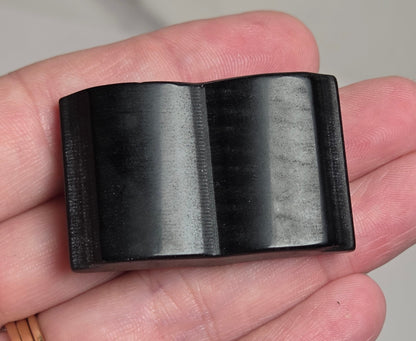 A black rectangular plastic component with a molded center ridge, held in a person's hand.