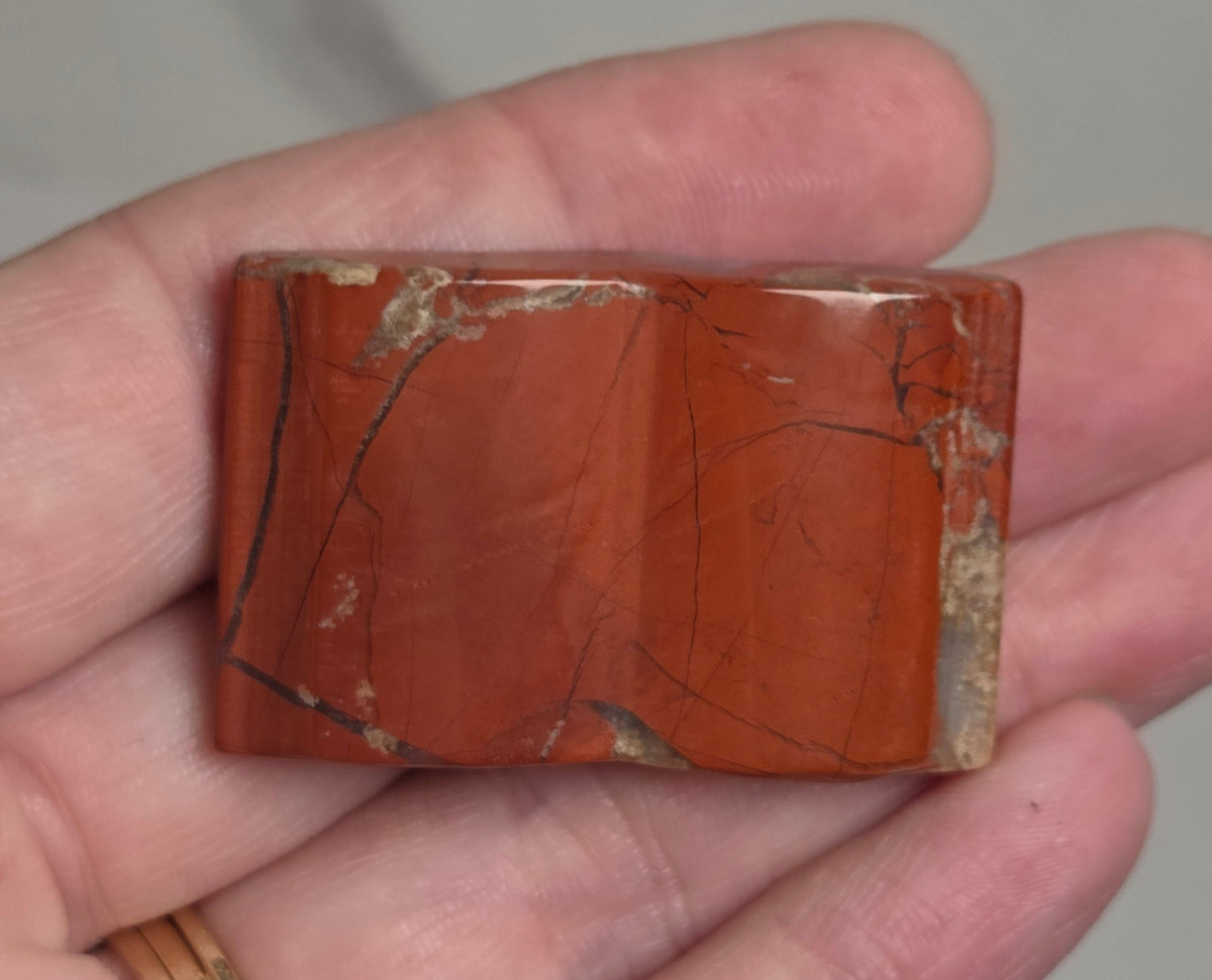 A rectangular reddish-brown stone or tile with natural fissures and light matrix, held in a person's hand against a light gray marble-like background.
