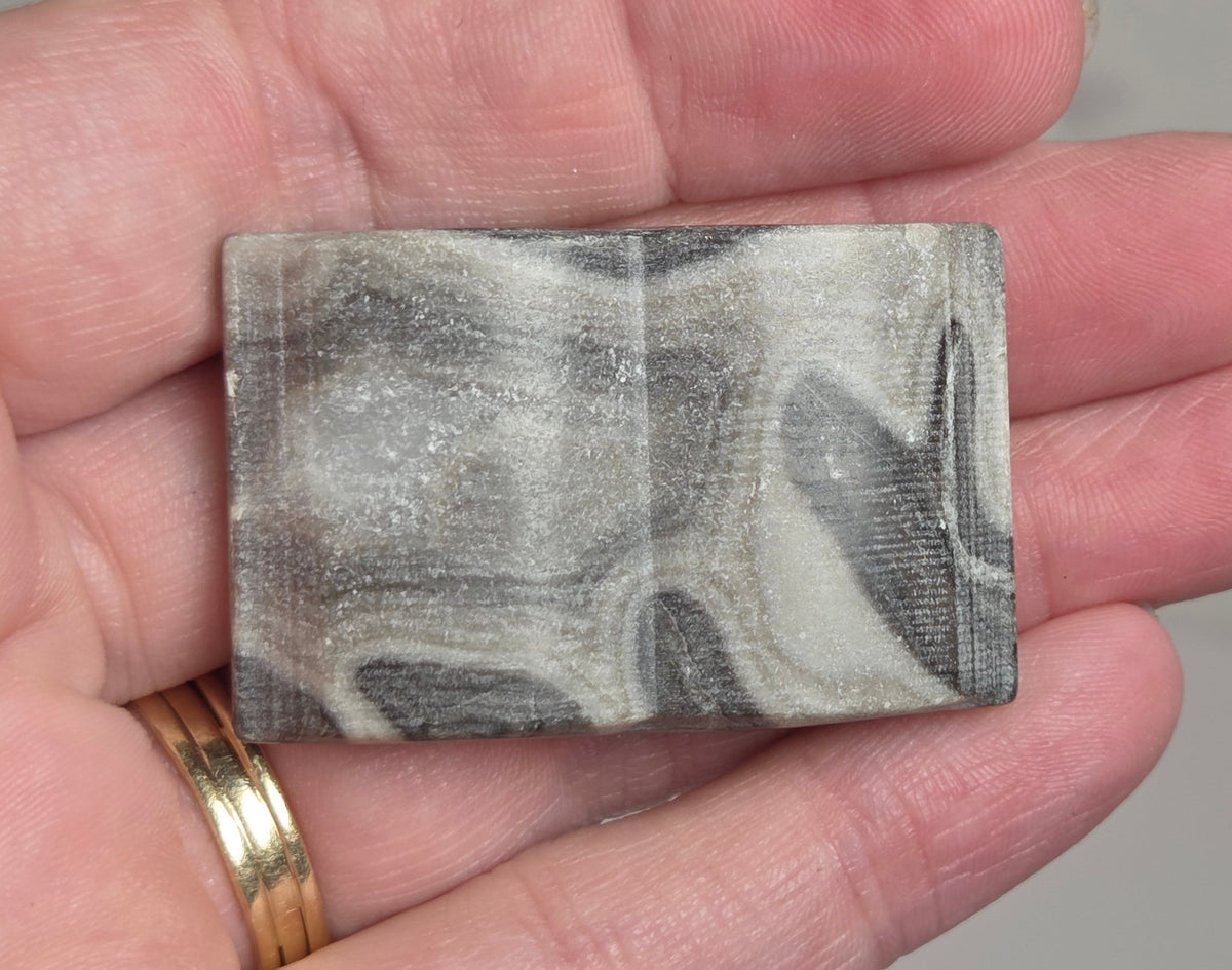 A rectangular stone or tile with a marbled gray, white, and black pattern, held in a person's hand.