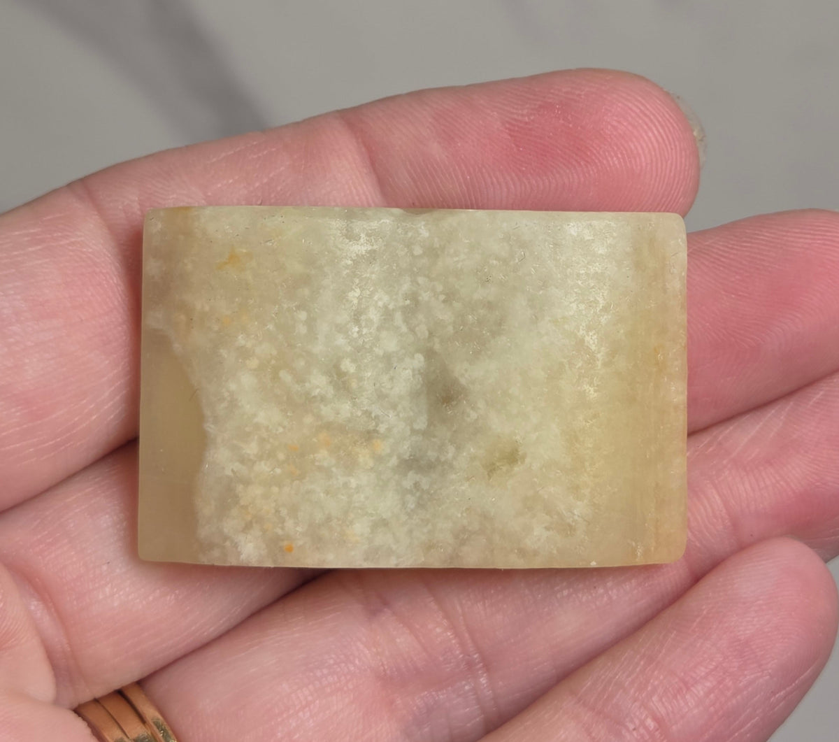 A rectangular pale yellow stone or resin bar held in a person's hand against a light marble-like background.
