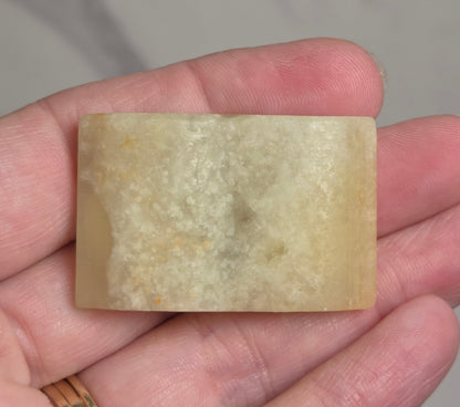A rectangular pale yellow stone or resin bar held in a person's hand against a light marble-like background.