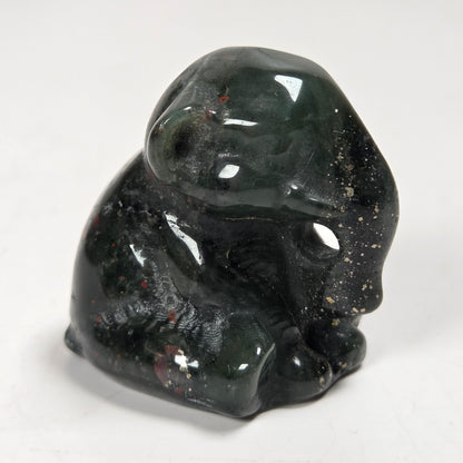 A small polished dark green stone figurine of a seated elephant shown on a plain light background.