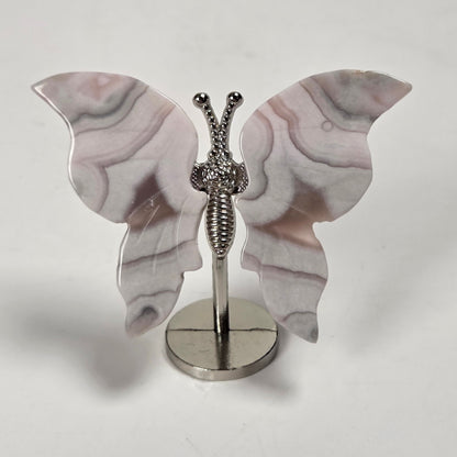 A butterfly-shaped jewelry display stand or decorative piece with pale pink and gray marbled wings on a silver metal stand, photographed against a plain light background.