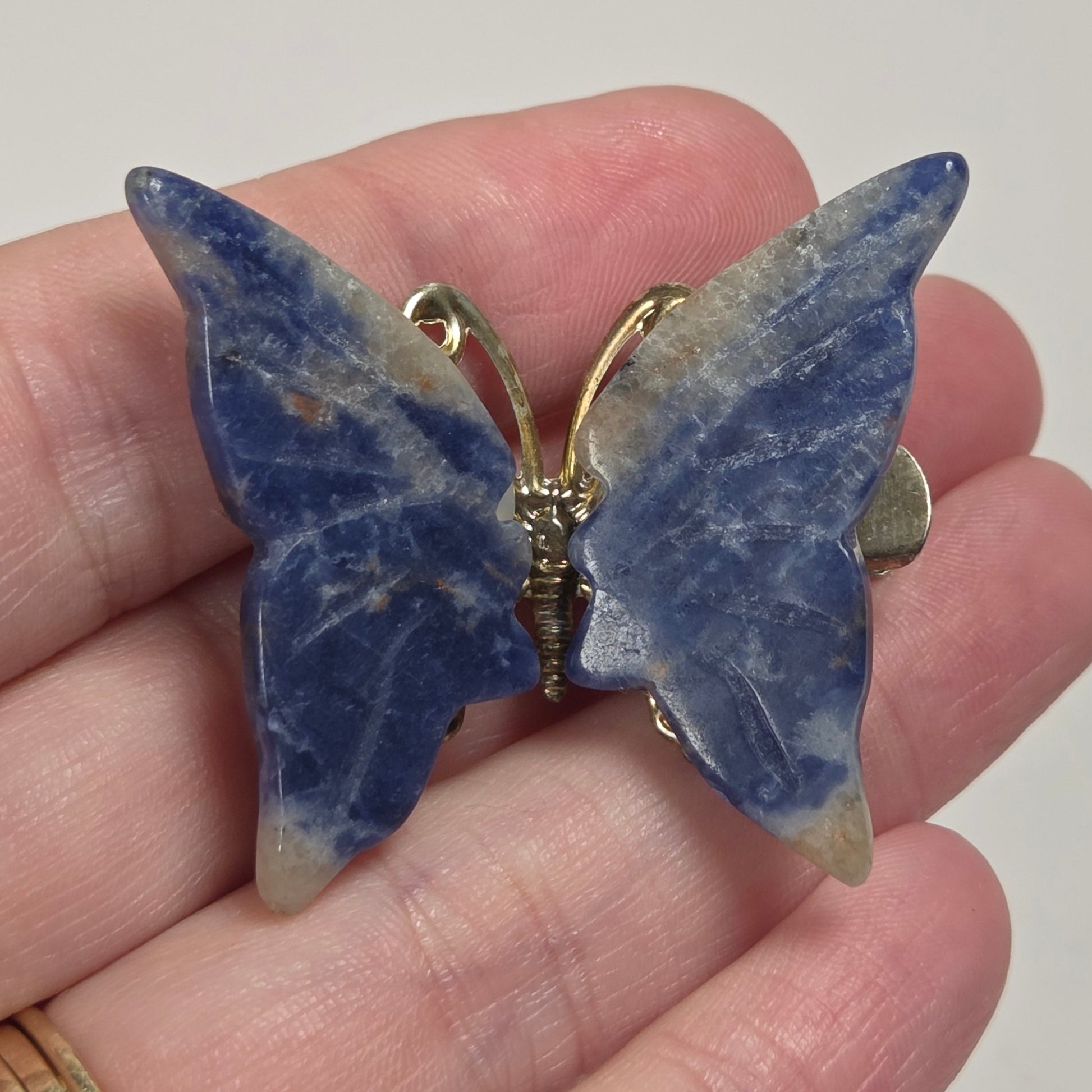 A butterfly-shaped brooch made of blue lapis lazuli stone with gold-tone metal accents, held on a person's hand.