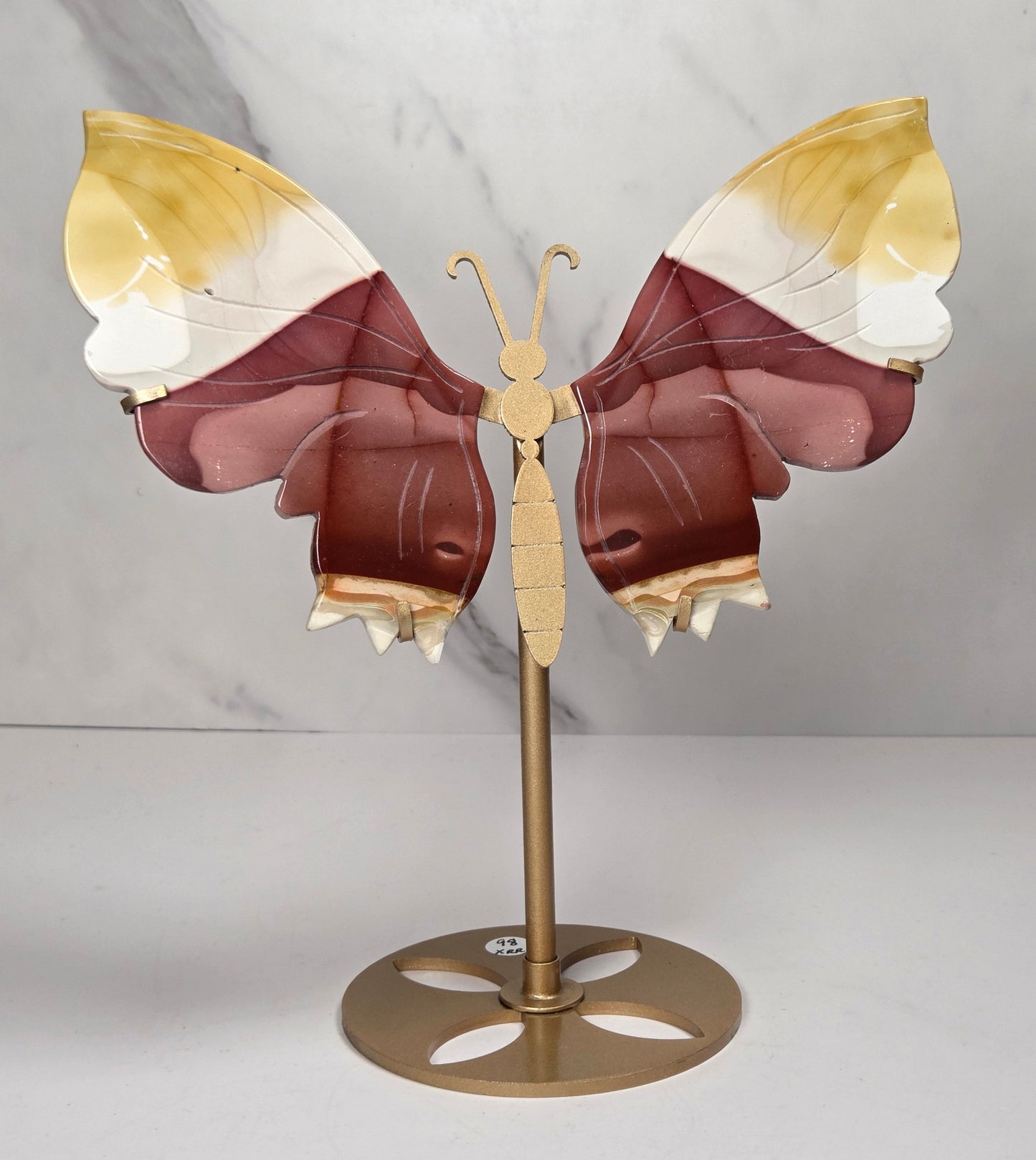 mookaite crystal carved butterfly wings on a gold stand against a marble background