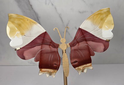 mookaite crystal carved butterfly wings on a gold stand against a marble background