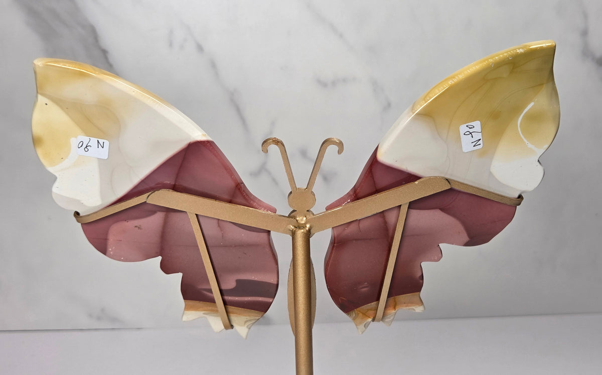 mookaite crystal carved butterfly wings on a gold stand against a marble background