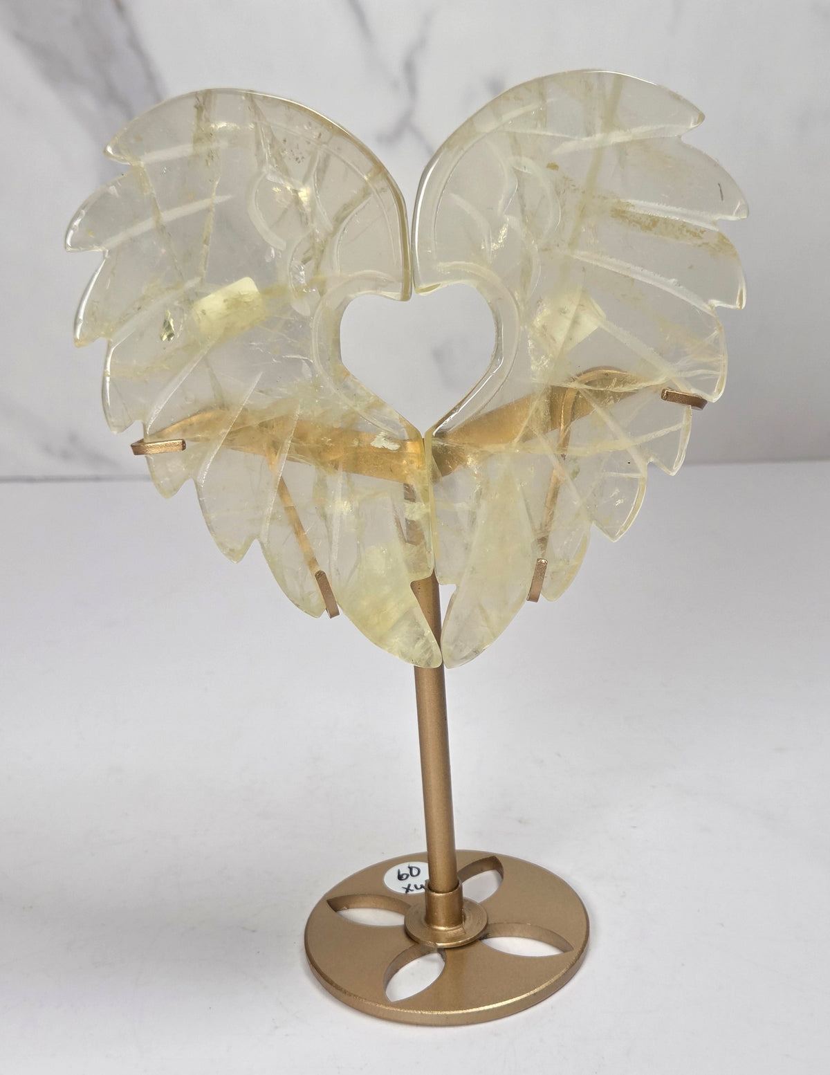 Carved Citrine wings that are in the shape of a heart, on a gold stand against a marbled background