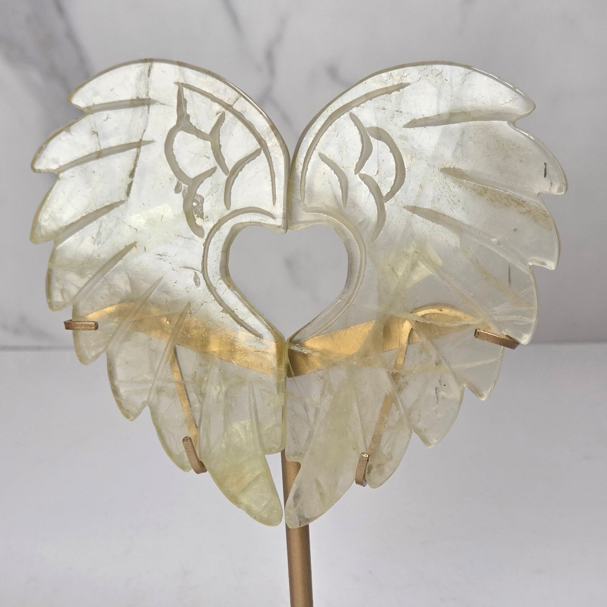 Carved Citrine wings that are in the shape of a heart, on a gold stand against a marbled background
