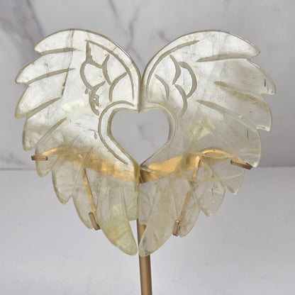 Carved Citrine wings that are in the shape of a heart, on a gold stand against a marbled background